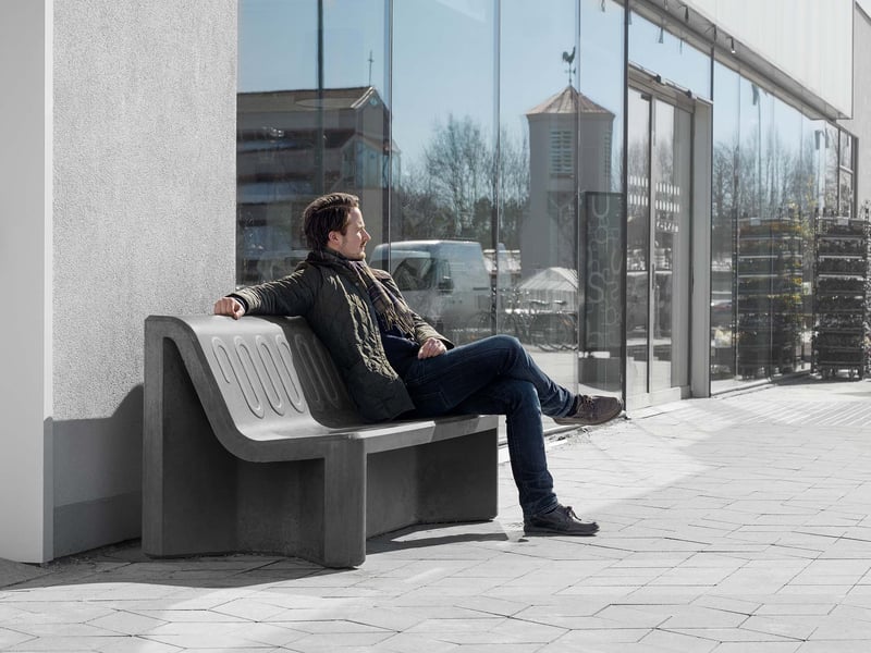 Person sittande i solsken på bänk av formgjuten betong